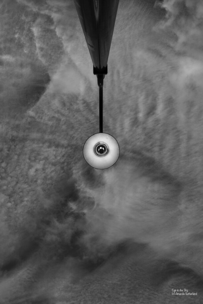 Black-and-white photograph looking upward at a streetlight surrounded by textured clouds, titled Eye in the Sky.
