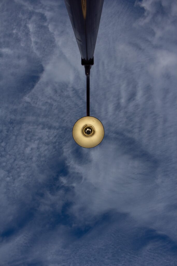 Colour photograph looking upward at a glowing streetlight surrounded by reflections of blue sky and white clouds.
