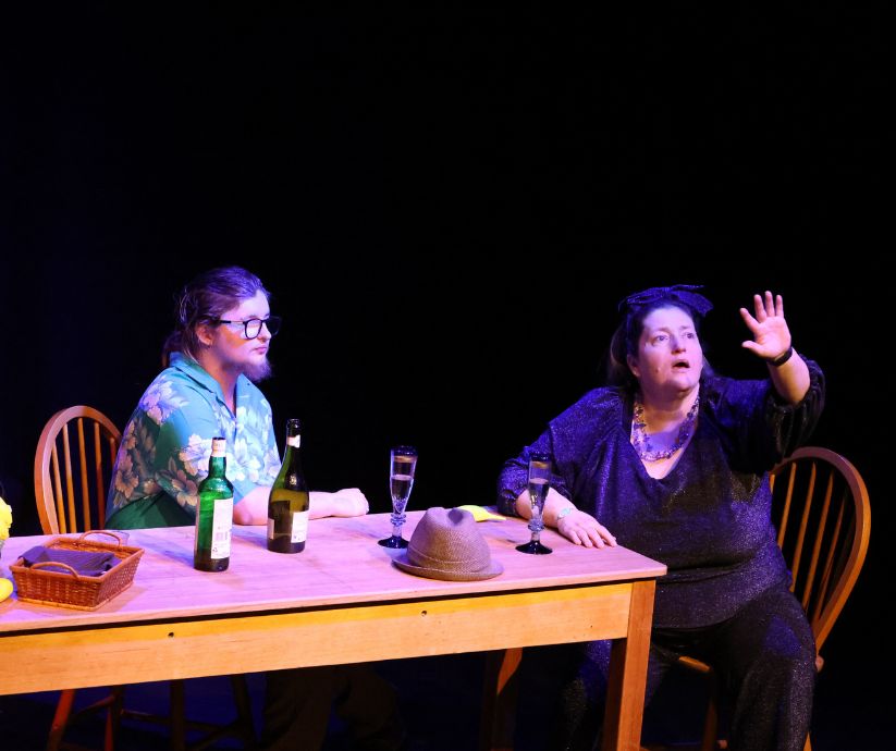 Amanda Sutherland as Ruth raising her hand and looking into the distance while Elliot Howe as Len sits beside her during The Banana Bender.